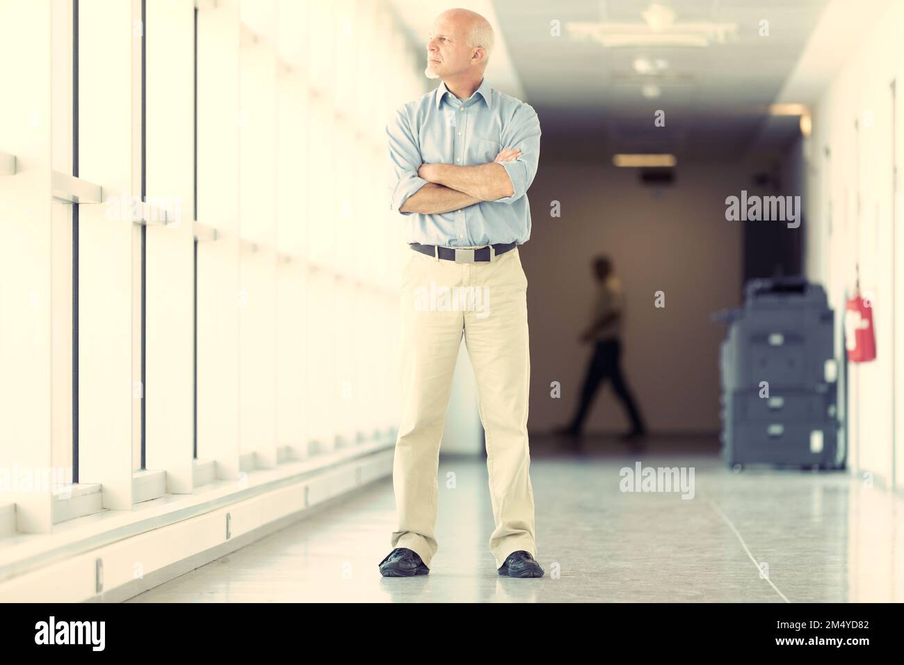 Strong elderly man on farm looks out the window. He has a proud posture and arms folded, dark shoes with light-colored pants. He dresses sporty and je Stock Photo
