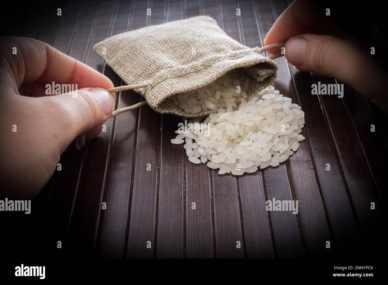 Hand holding straw pouch full of uncooked rice on a wooden background ...