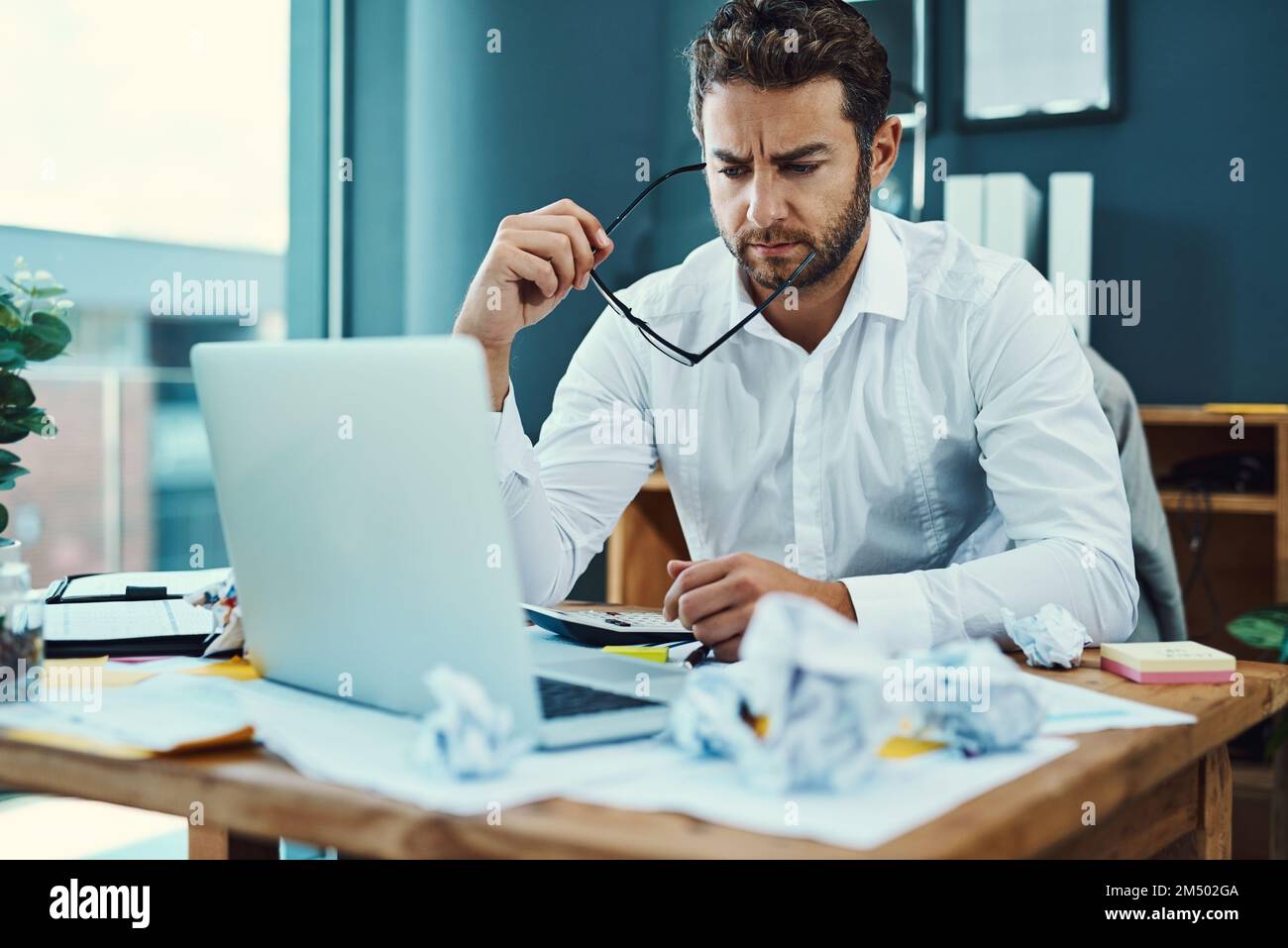 Theres a problem that he just cant figure out. a young businessman looking serious while working on a laptop in an office. Stock Photo