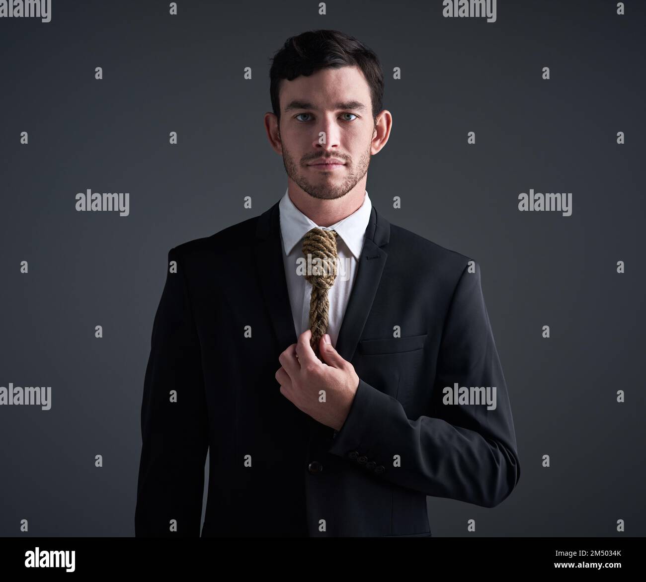 Where a necktie or a noose. Its your choice. Studio portrait of a young businessman with a noose tied around his neck for a tie against a gray Stock Photo
