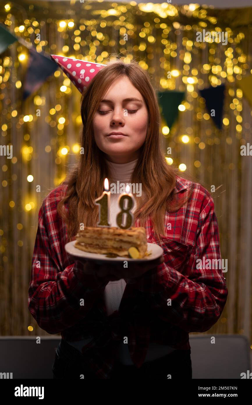 Birthday celebration. Happy 18 years old girl in party cone make a wish