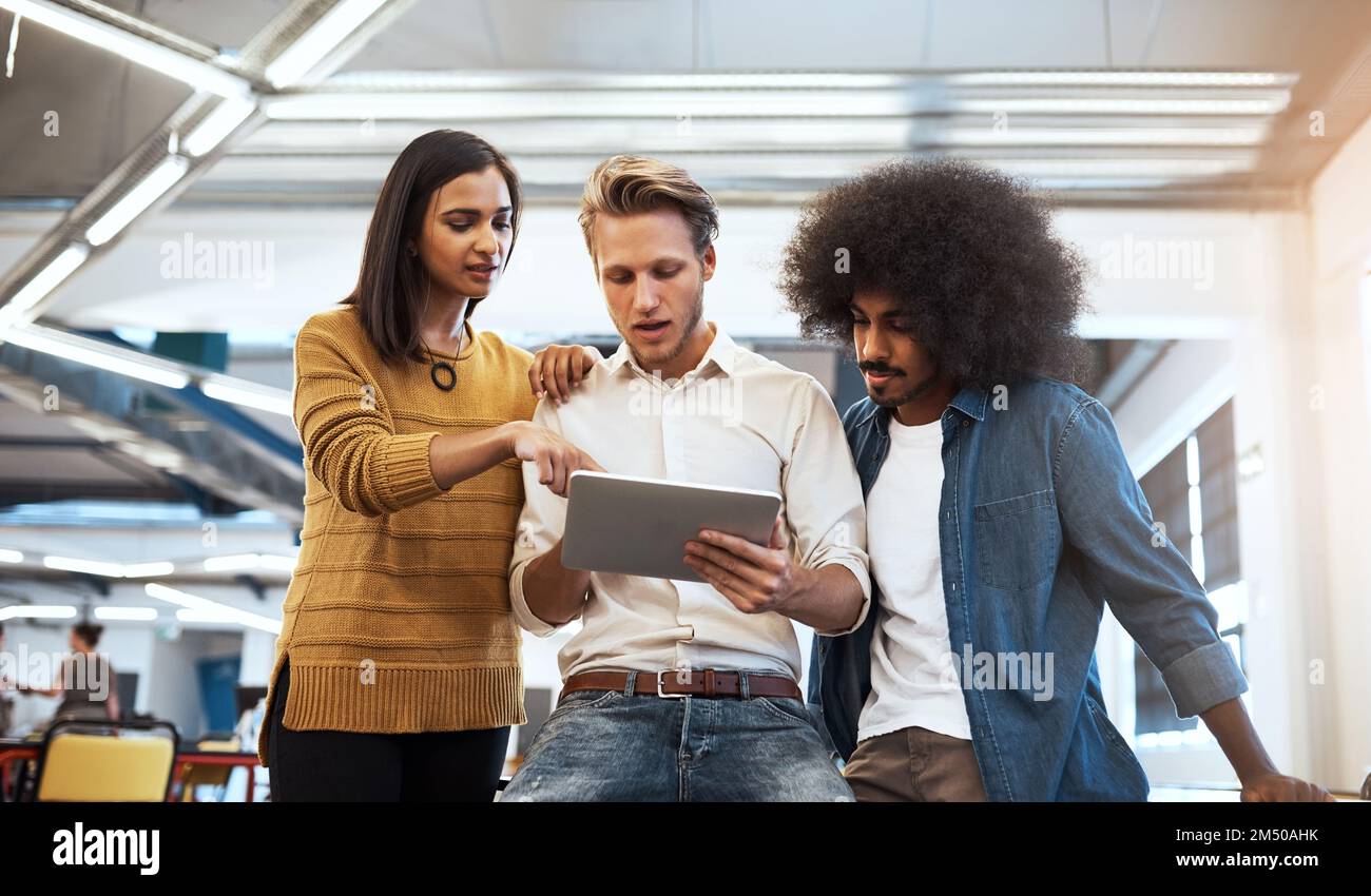 Getting some much needed input. three young businesspeople looking at a tablet in their office. Stock Photo