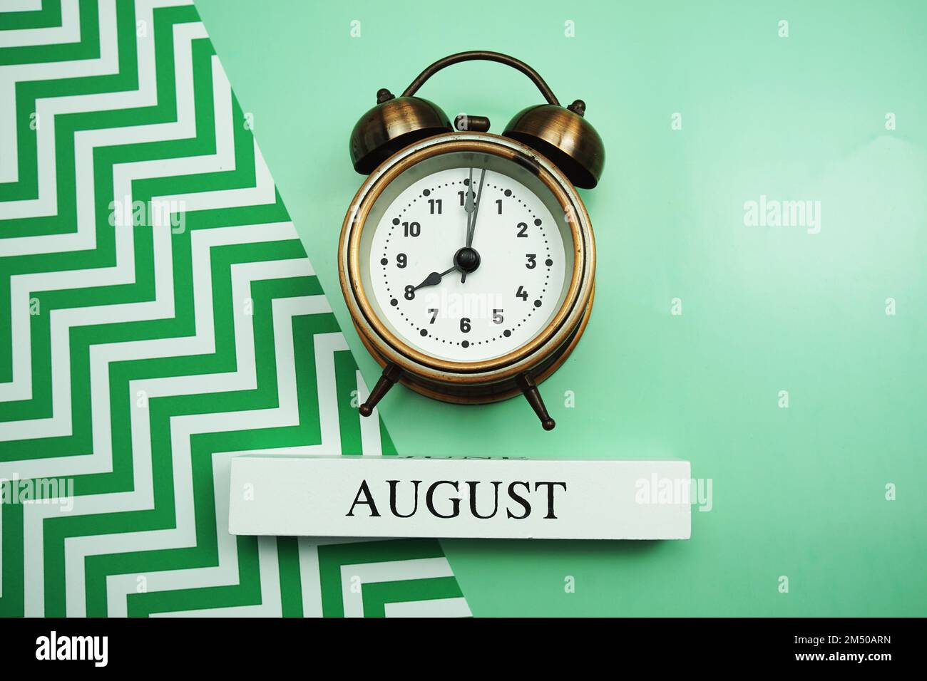 August and alarm clock on green background Stock Photo - Alamy