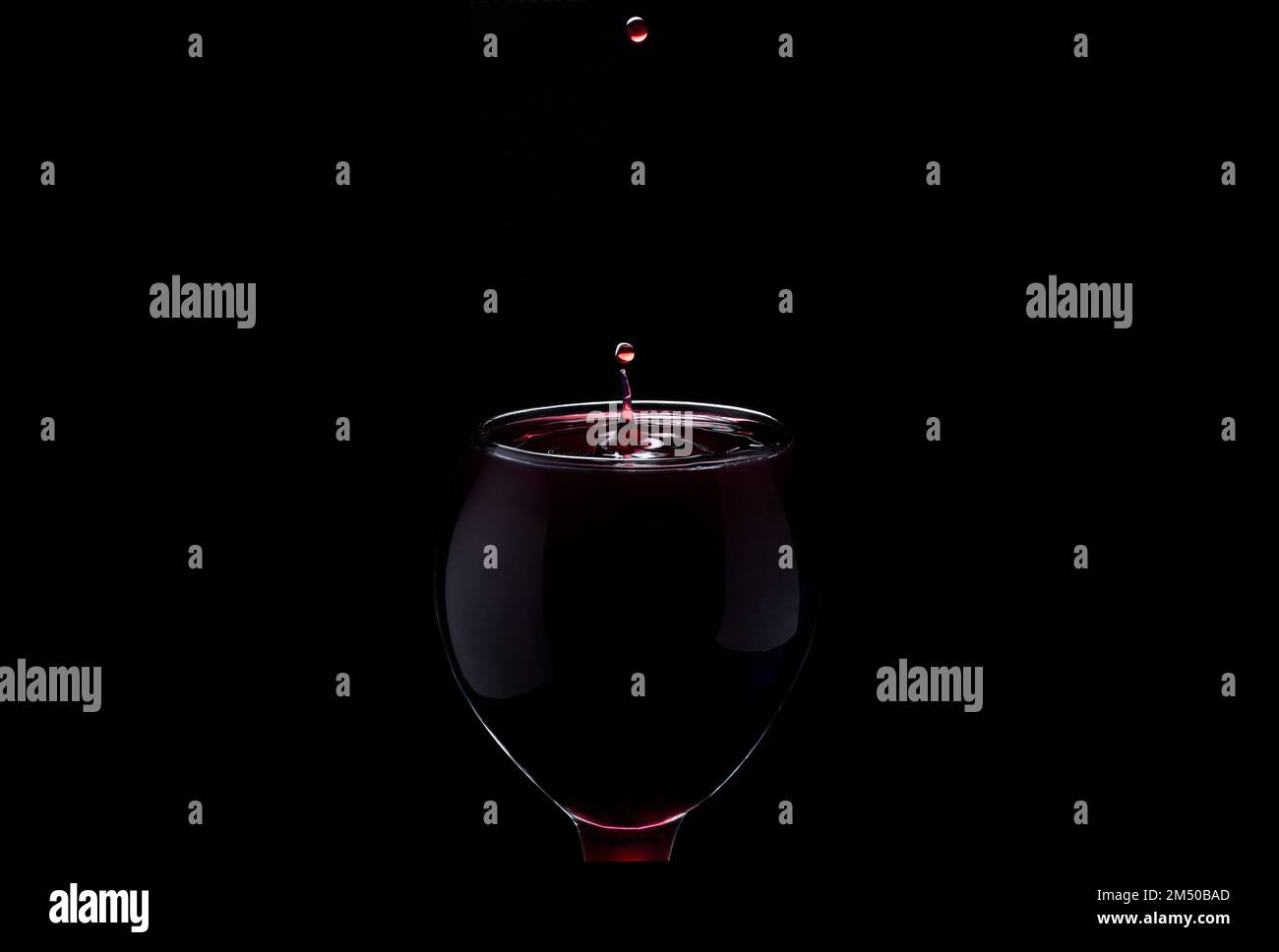 A closeup shot of a waterdrop falling into a glass with red liquid, making concentric circles on a black background, the concept of drinking Stock Photo