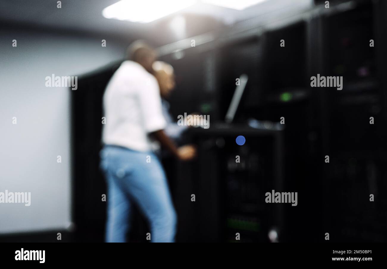 System administrators to the rescue. two IT technicians using a computer while working in a server room. Stock Photo