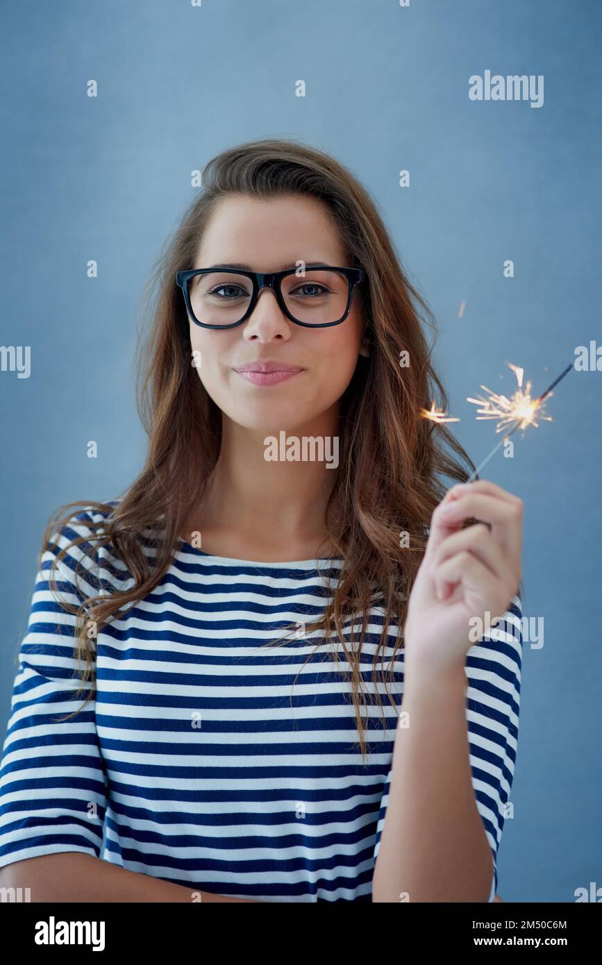 Dont be afraid to sparkle. Studio shot of a beautiful young woman holding sparklers against a blue background. Stock Photo
