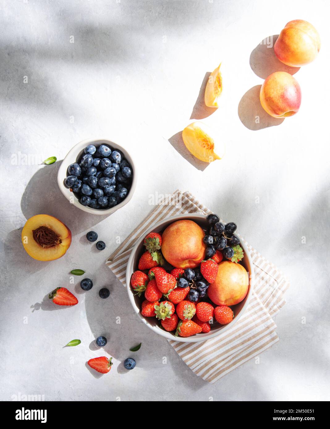 Fresh organic summer berries and fruits of strawberries, blueberries, peaches and grapes in a white plate on a light background with morning shadow. T Stock Photo