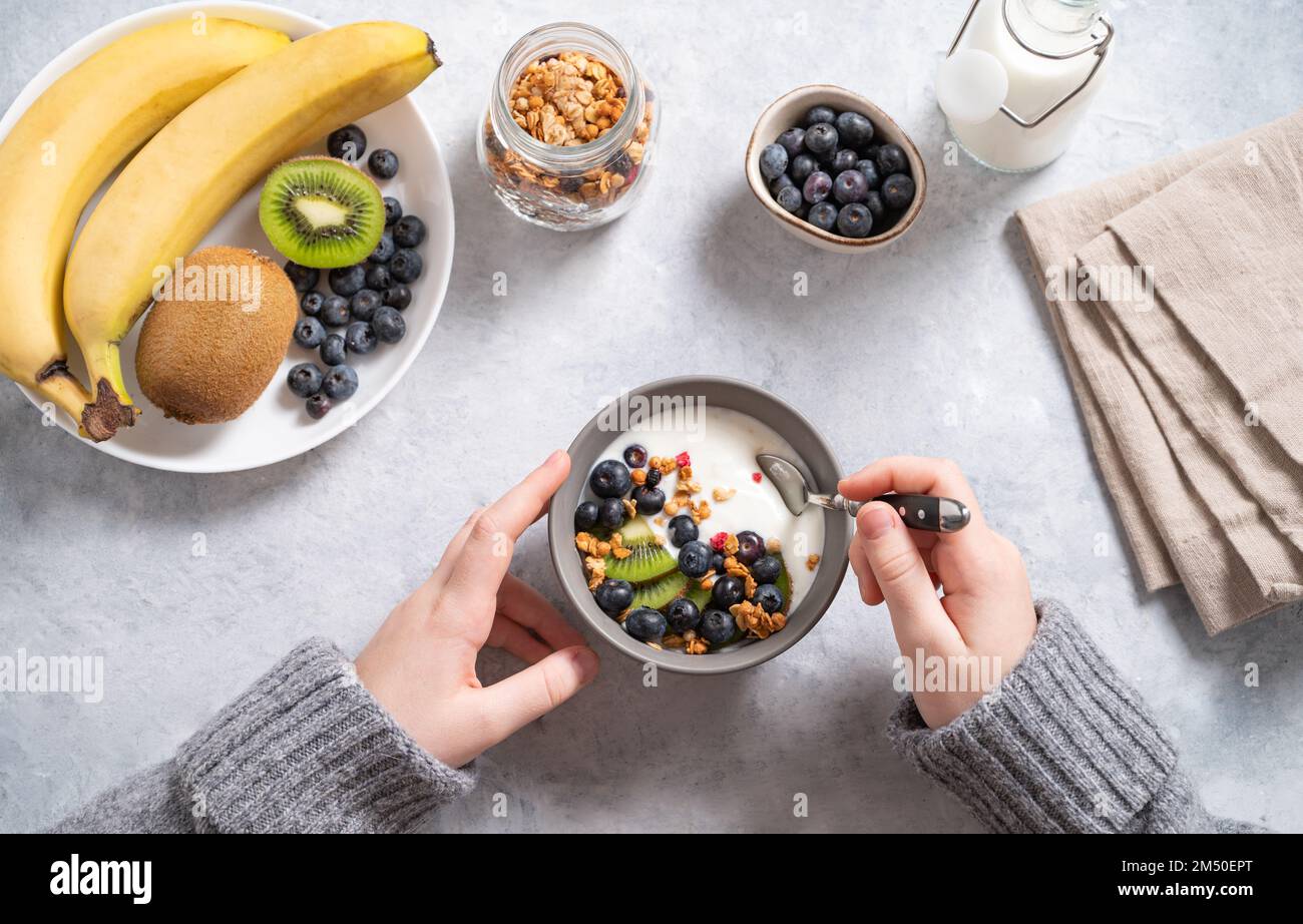 the child has breakfast with a hearty and healthy yogurt with granola and fresh fruits and berries. Top view. Stock Photo