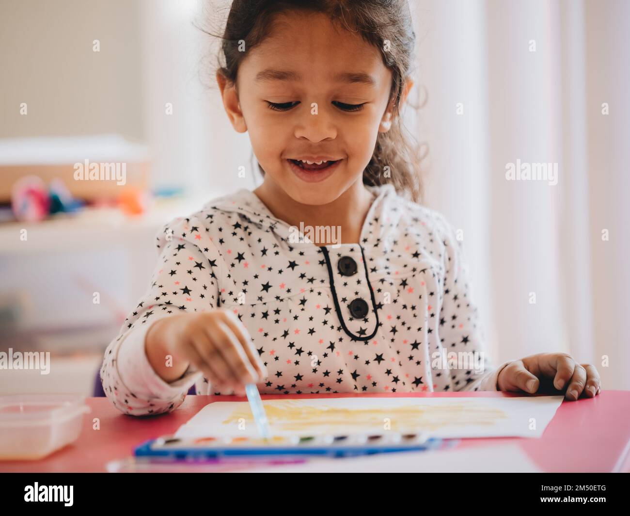 A cute preschool girl at home painting with watercolors on a piece of ...