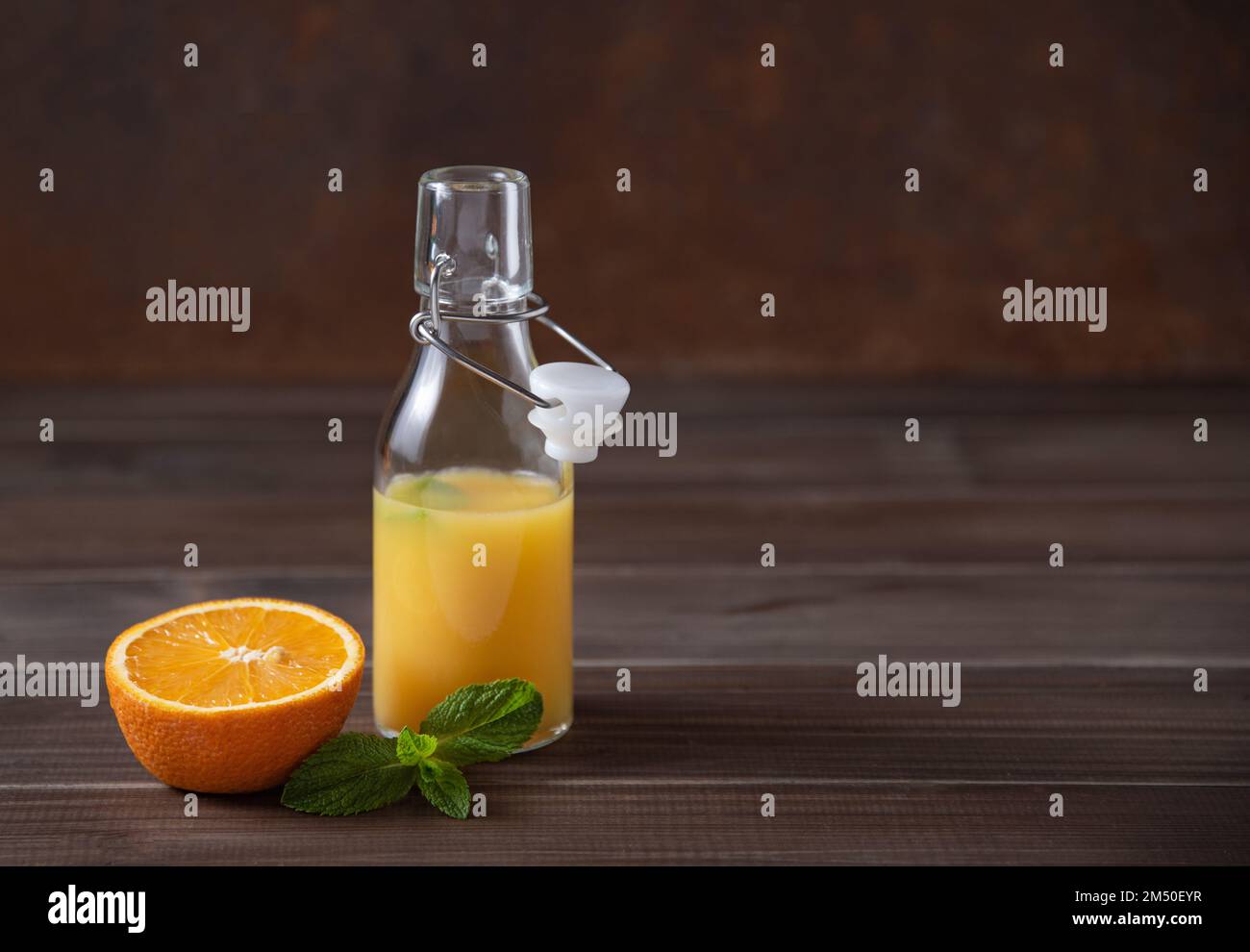Fresh orange juice in bottle with citrus fruit and mint  on a brown wooden background. Rustic minimalism concept. Front view and copy space image Stock Photo