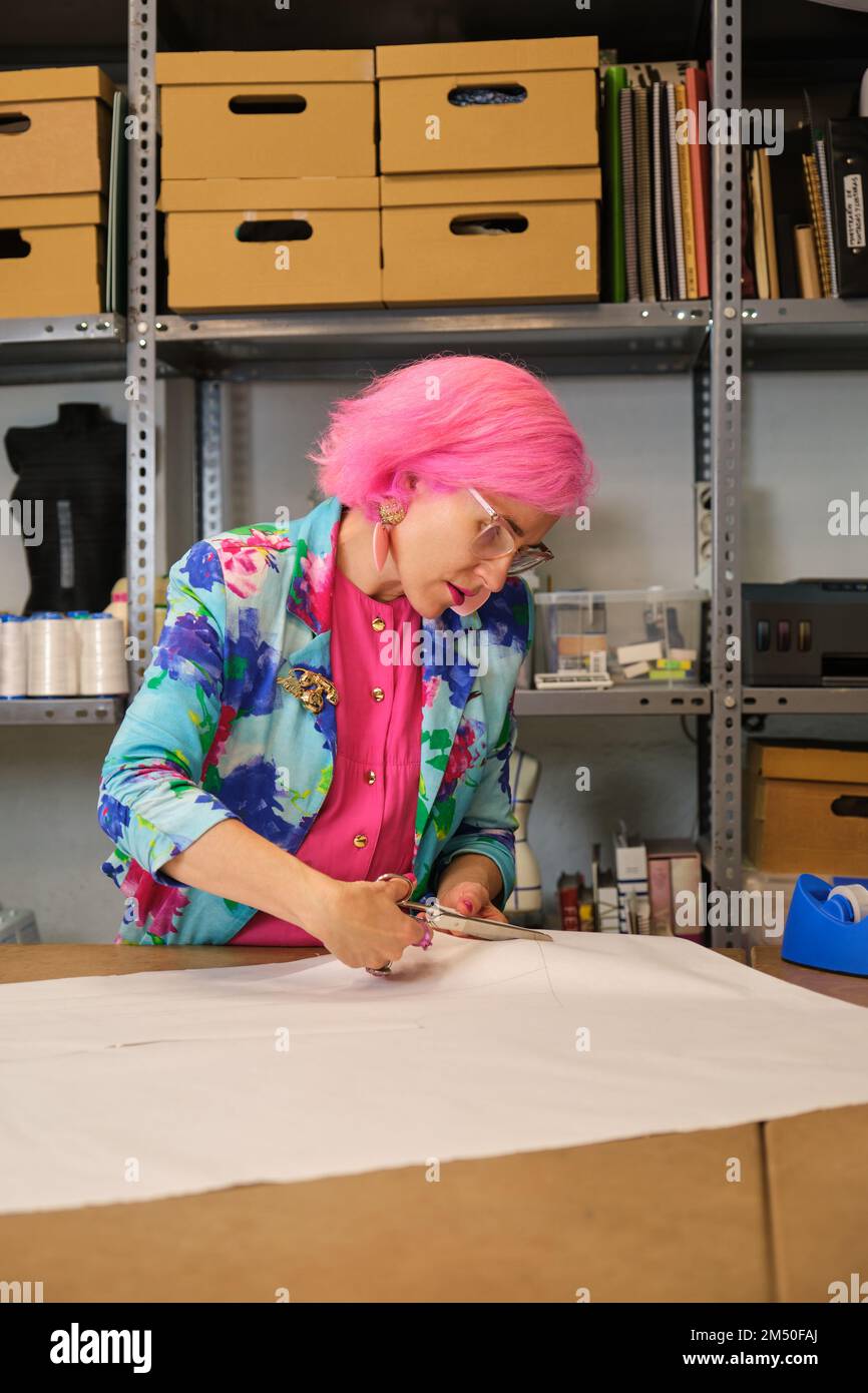 Seamstress with pink hair and colorfull clothes cutting sewing patterns. Stock Photo