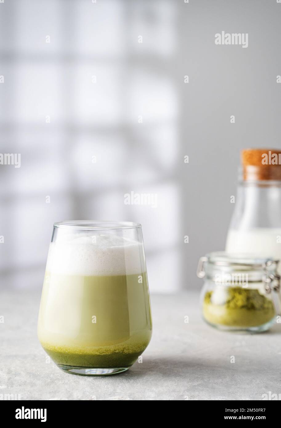Green matcha latte in a glass on a gray background with morning shadows from the window, a bottle of milk and tea powder The concept of a vegan drink, Stock Photo
