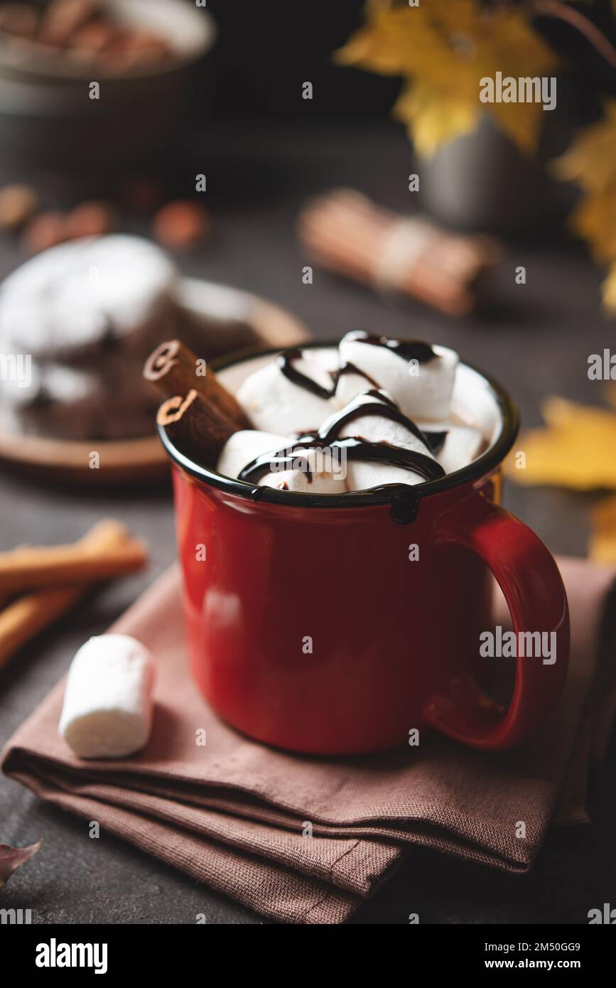 Red cup of hot chocolate with marshmallow and cinnamon on a dark brown table with maple leaves and cookies. Autumn concept of a  warming     drink. Ti Stock Photo