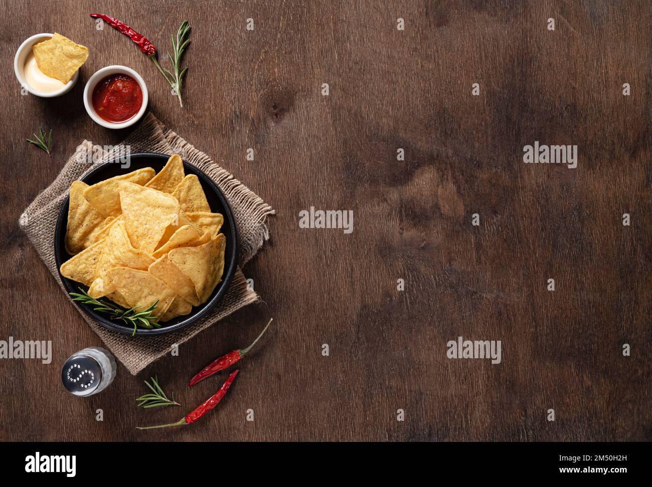 Traditional Mexican corn chips nachos with salsa and cream sauce, herbs, salt and chili pepper on a wooden background. Top view and copy space. Stock Photo