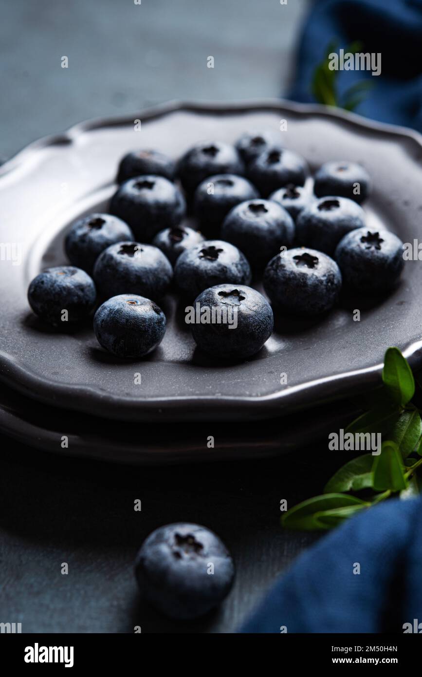 Juicy and ripe blueberries on a gray plate on a dark blue background with a napkin. Close up and macro view. Stock Photo