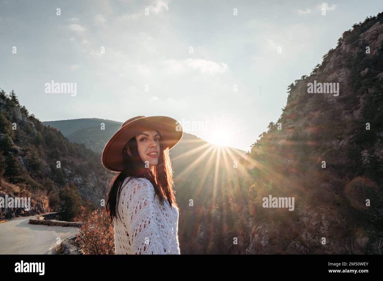Traveler woman in brown hat and white sweater looking at amazing mountains and forest, wanderlust travel concept, atmospheric epic moment Stock Photo