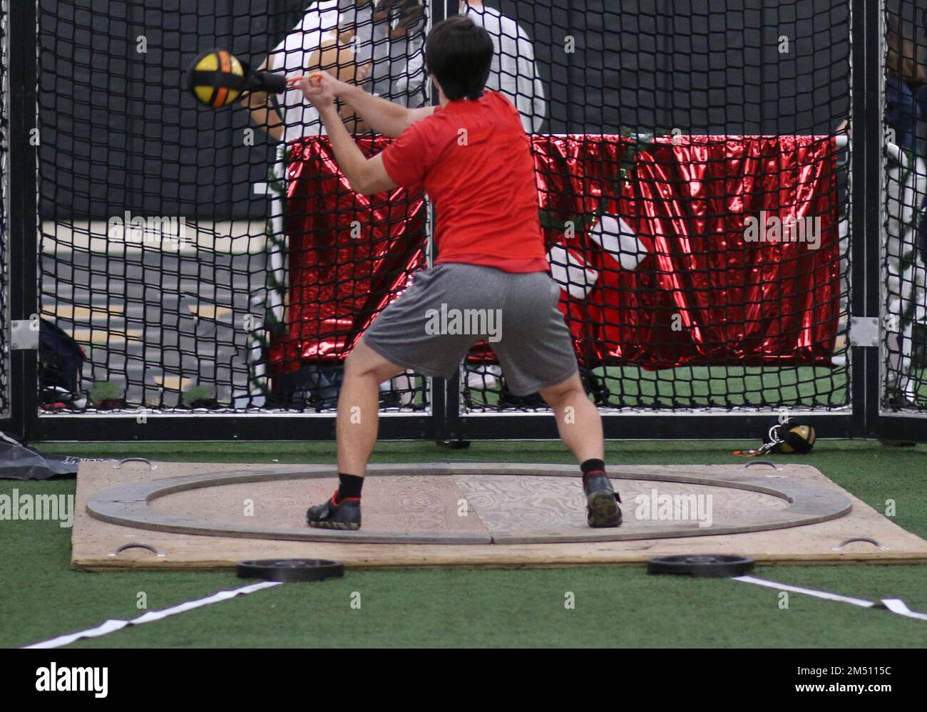 A high school boy throwing the weight indoor during a track and field weight throw competition. Stock Photo