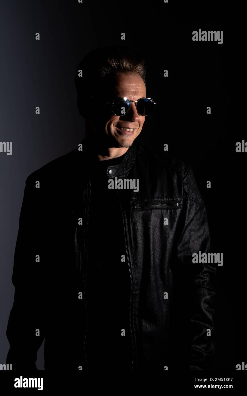 Portrait of handsome male. Sexy stylish man dressed in a leather jacket and sunglasses. Fashion hipster male isolated on grey background in studio Stock Photo