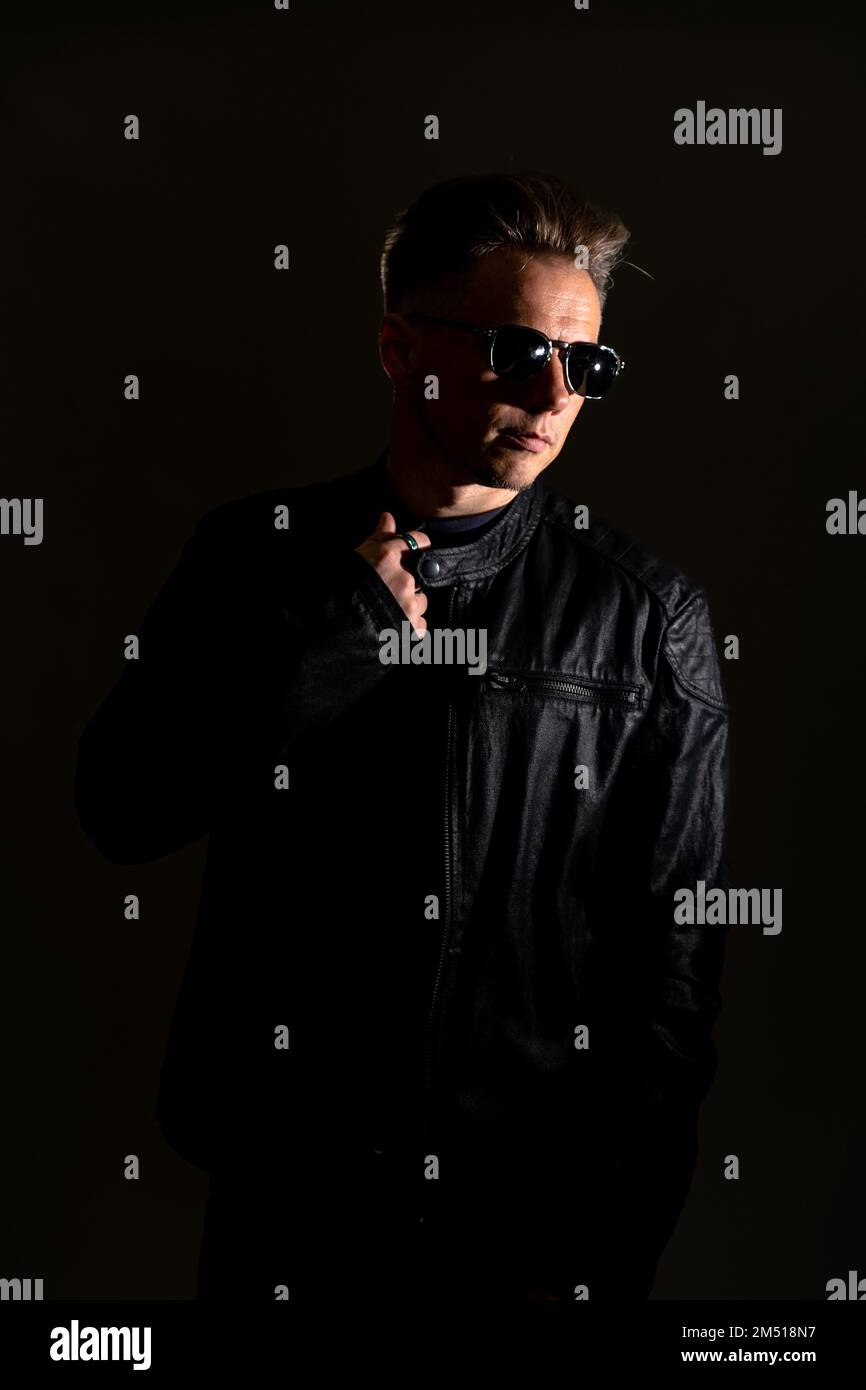 Portrait of handsome male. Sexy stylish man dressed in a leather jacket and sunglasses. Fashion hipster male isolated on grey background in studio Stock Photo