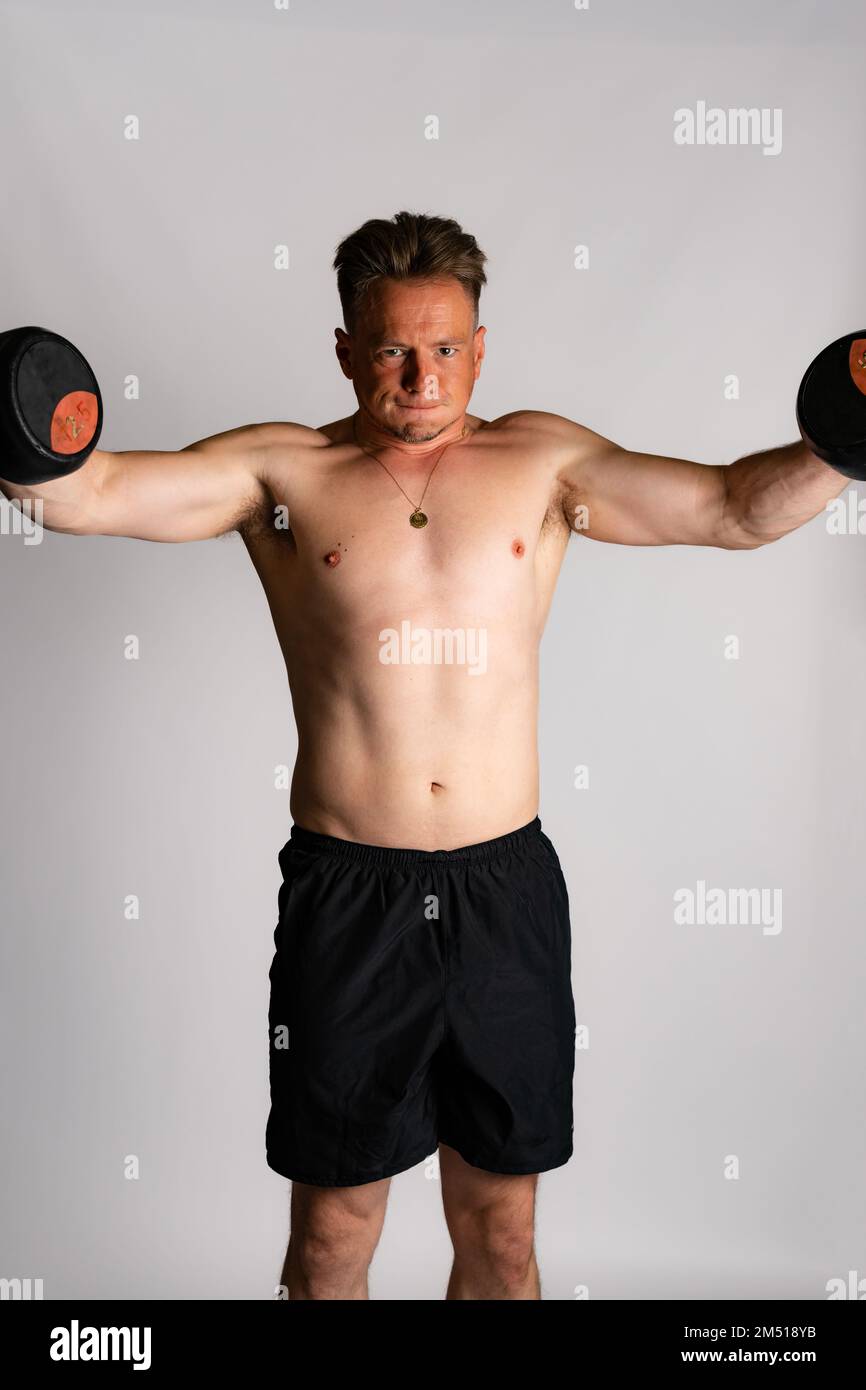 Athletic man weightlifting or power lifting, working on arms and chest muscles with heavy dumbbells. Muscular shirtless handsome man Stock Photo