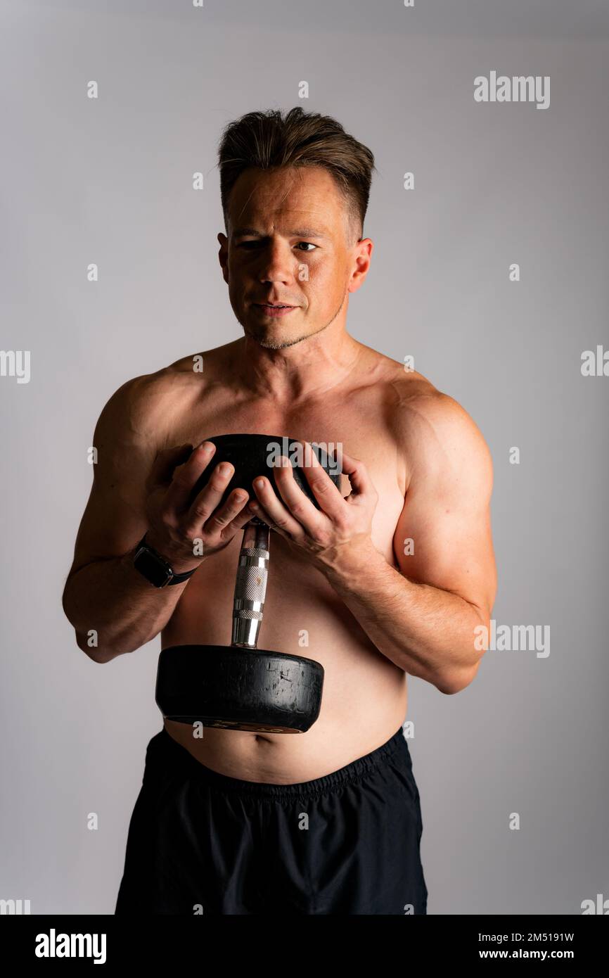Athletic man weightlifting or power lifting, working on arms and chest muscles with heavy dumbbells. Muscular shirtless handsome man Stock Photo