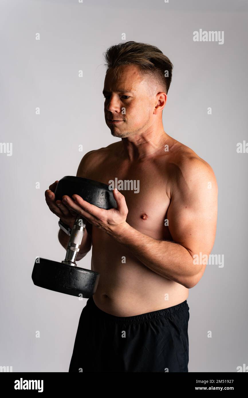 Athletic man weightlifting or power lifting, working on arms and chest muscles with heavy dumbbells. Muscular shirtless handsome man Stock Photo