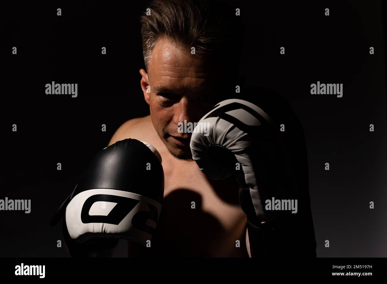 Portrait of muscular handsome topless male wearing boxing gloves isolated against a black background Stock Photo