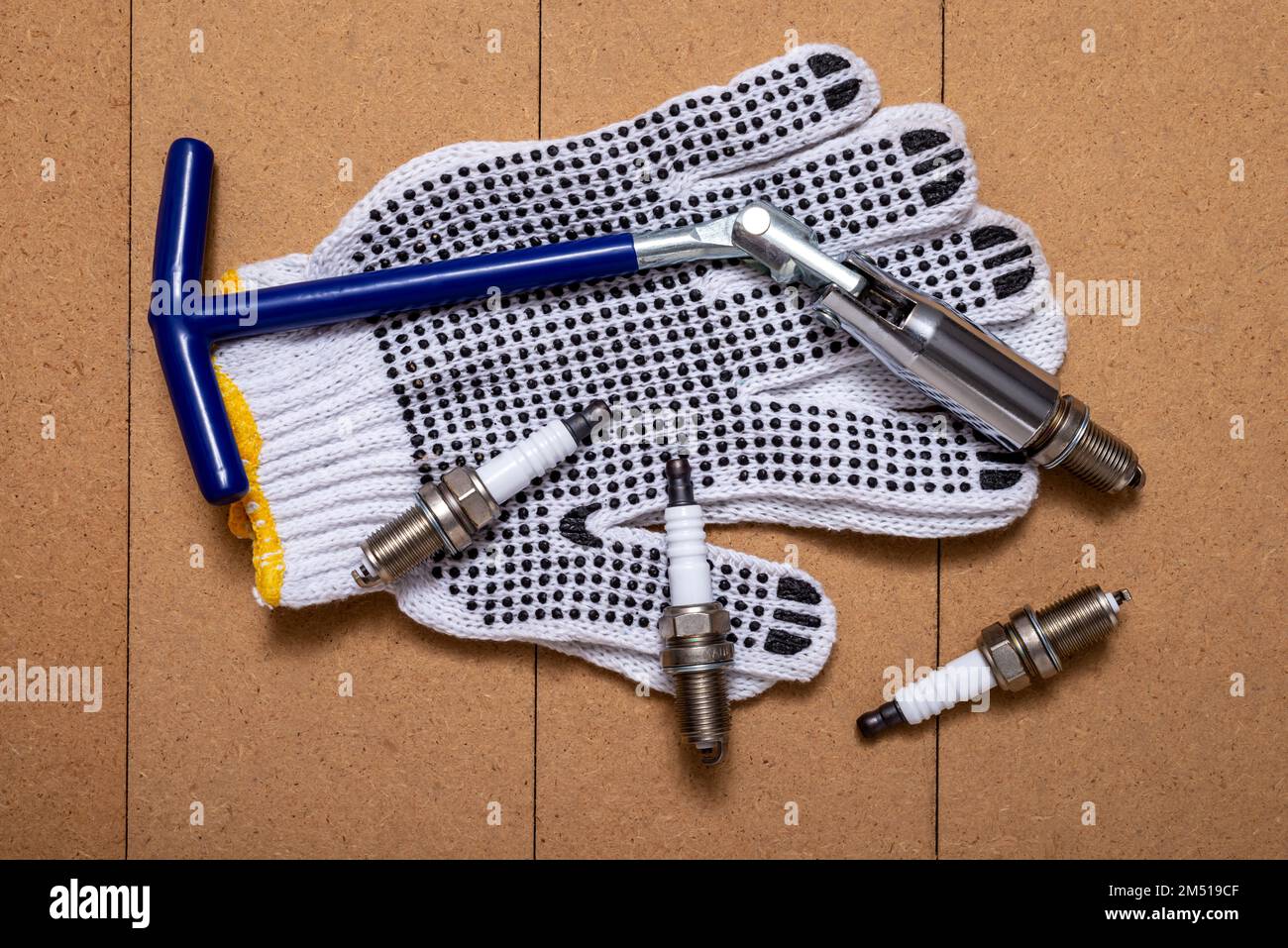 Sparking plugs, spark plug key and protective gloves on wooden table. Stock Photo