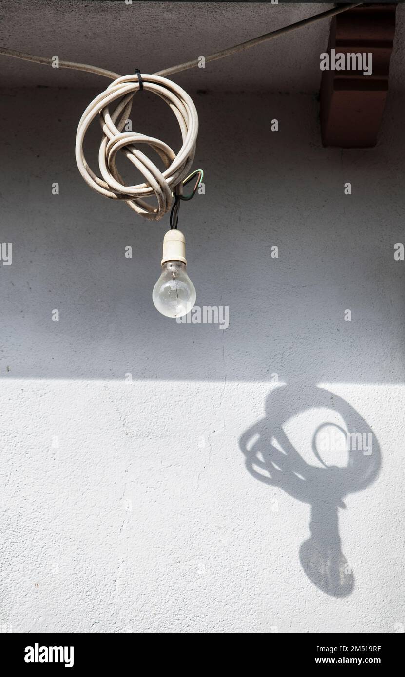 Old light bulb hanging from a ledge with the excess cord coiled up. Perfect shadow on wall Stock Photo
