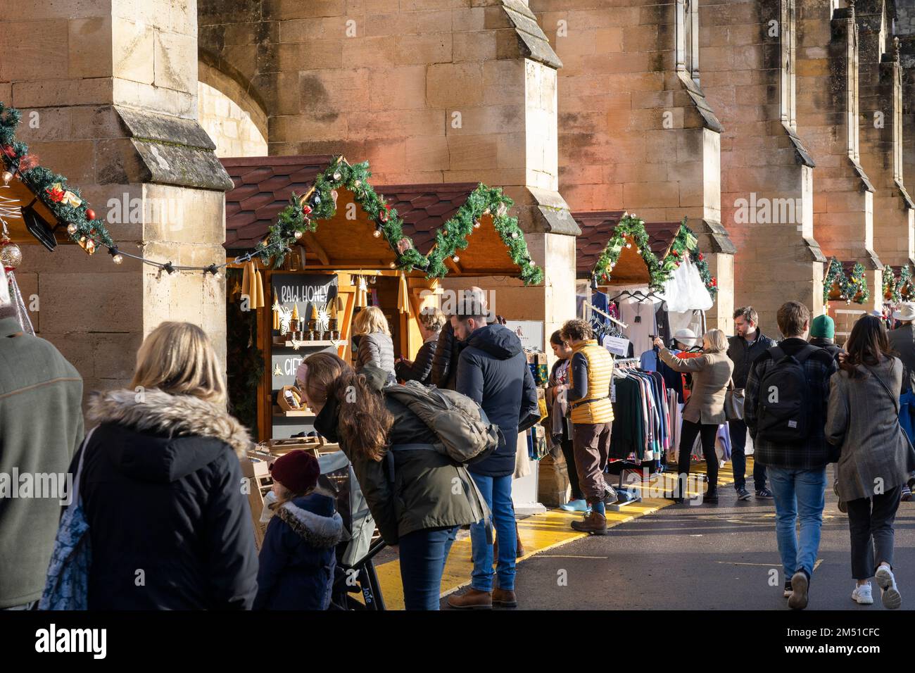 Christmas shoppers at Winchester Christmas market with stalls inbetween stone flying buttresses of Gothic Winchester Cathedral, England, UK Stock Photo