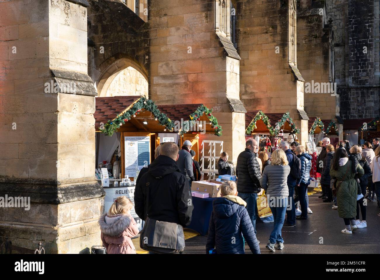 Christmas shoppers at Winchester Christmas market with stalls inbetween stone flying buttresses of Gothic Winchester Cathedral, England, UK Stock Photo