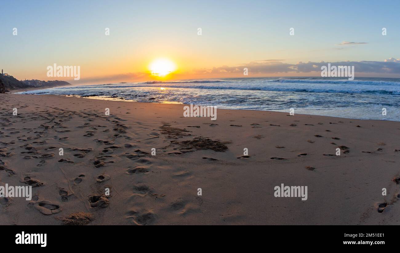 Beach sand ocean waters edge with sea waves at sunrise sunset over the horizon a beautiful natural coastline landscape. Stock Photo