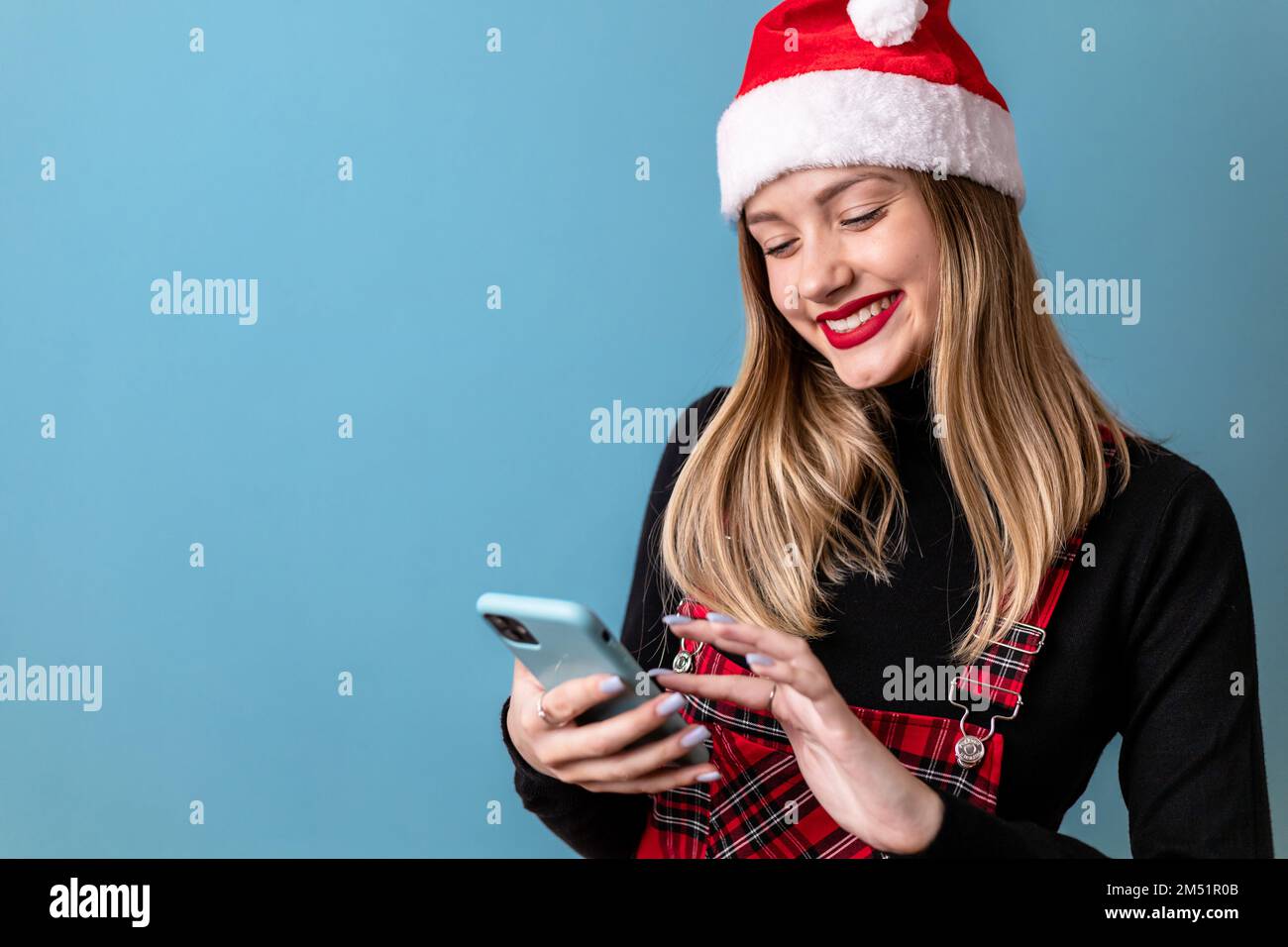 Young, blonde girl with Santa hat looking at her phone Stock Photo