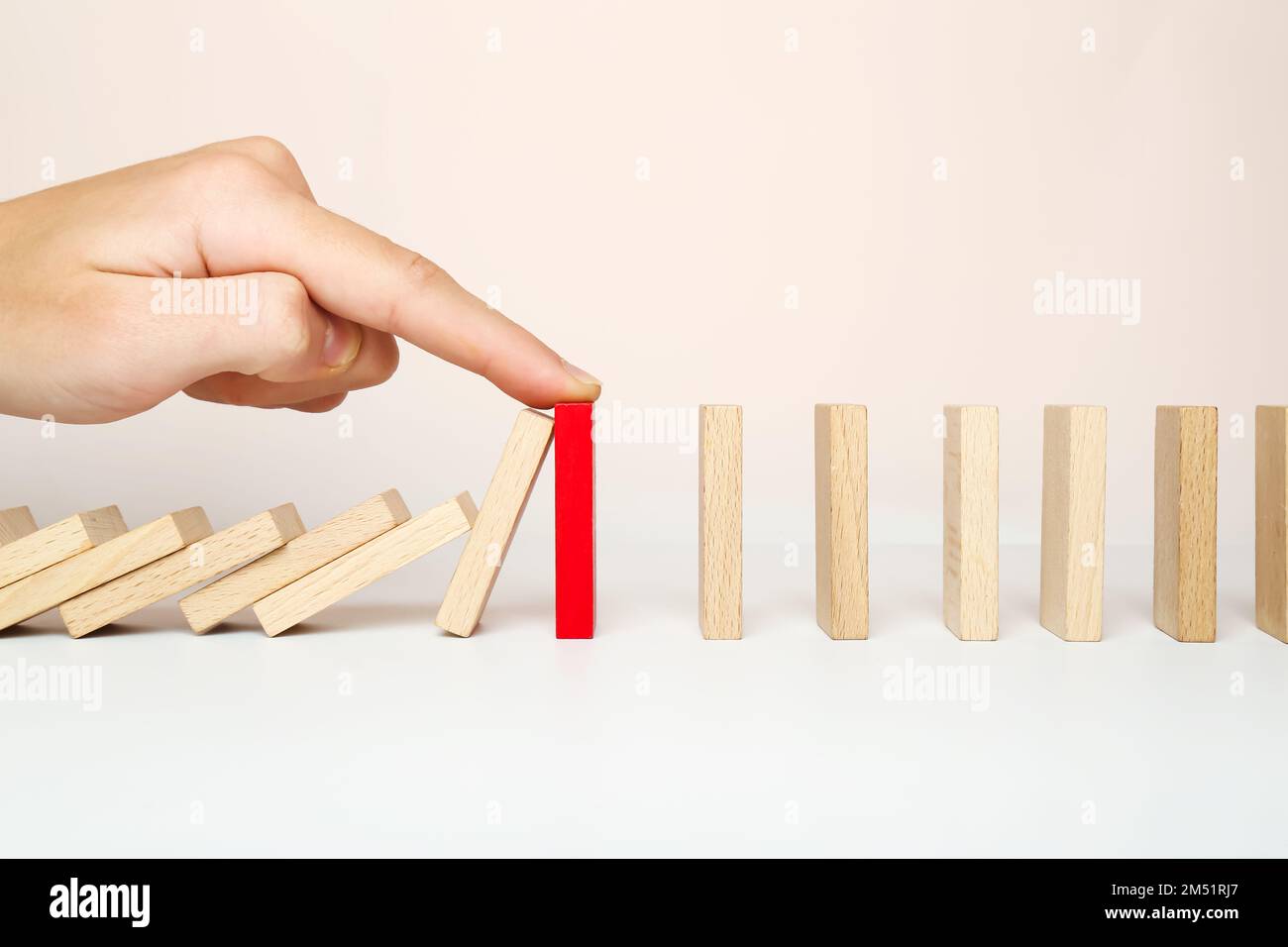 The domino falls, and the finger stops the chain reaction. The concept of solving the problem. Stock Photo