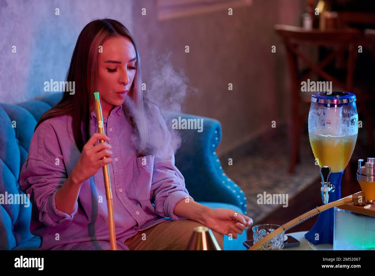 Portrait of young woman smoking hookah and drinking beer in bar when