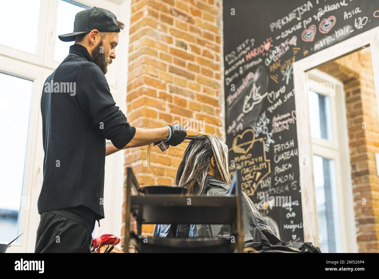 Hairdresser in the black clothes with beard wearing black gloves dyeing