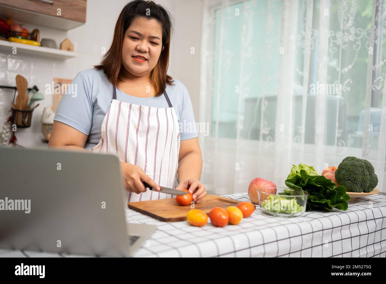 Asian Pregnant learn how to cook healthy meals from the Internet in kitchen, Fat women prepare a vegetable salad for diet food and lose weight. Concep Stock Photo