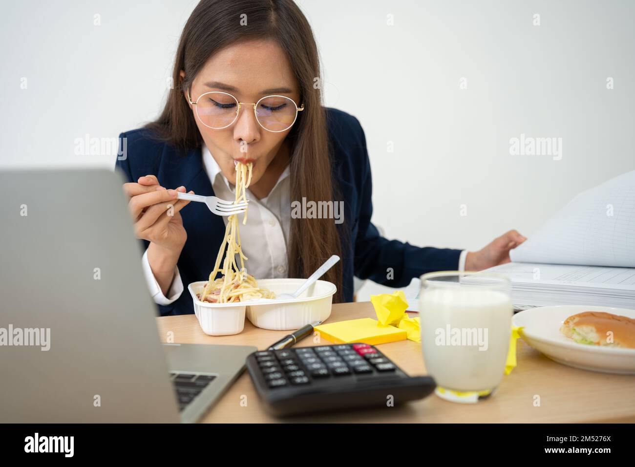 Busy and tired businesswoman eating spaghetti for lunch at the Desk office and working to deliver financial statements to a boss. Overworked and unhea Stock Photo