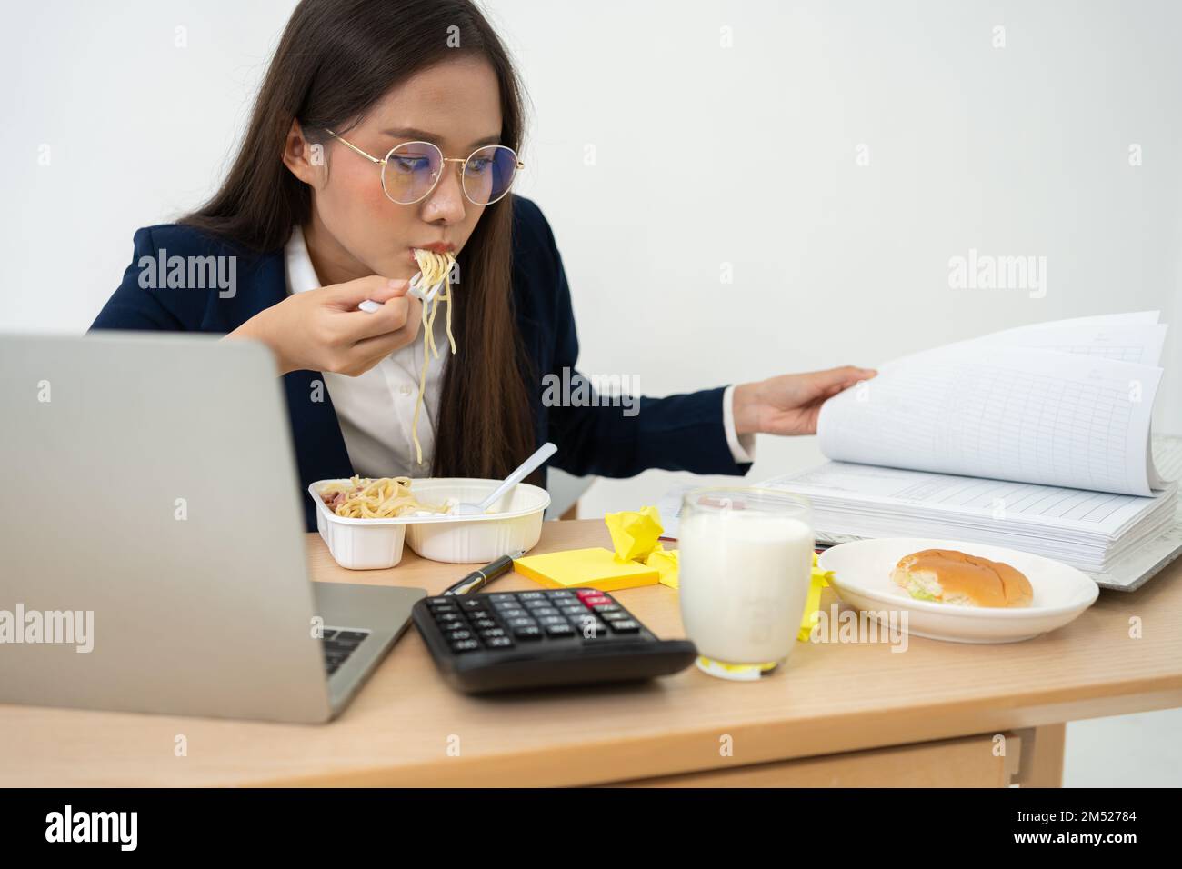Busy and tired businesswoman eating spaghetti for lunch at the Desk office and working to deliver financial statements to a boss. Overworked and unhea Stock Photo