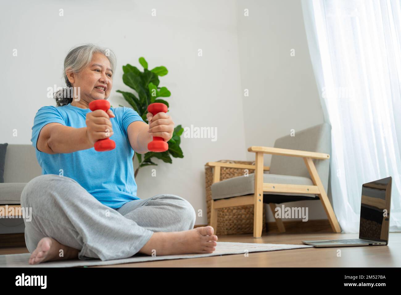 Asian senior woman lifting dumbbell for exercise and workout at home. Active mature woman doing stretching exercise in living room. Exercise Active an Stock Photo