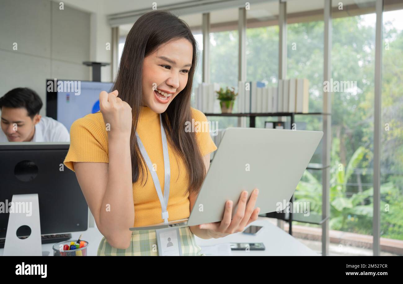 Young Asian Happy Businesswoman or intern using Computer in Modern Office background is Colleagues discuss with new startup project Idea. Empowered Di Stock Photo