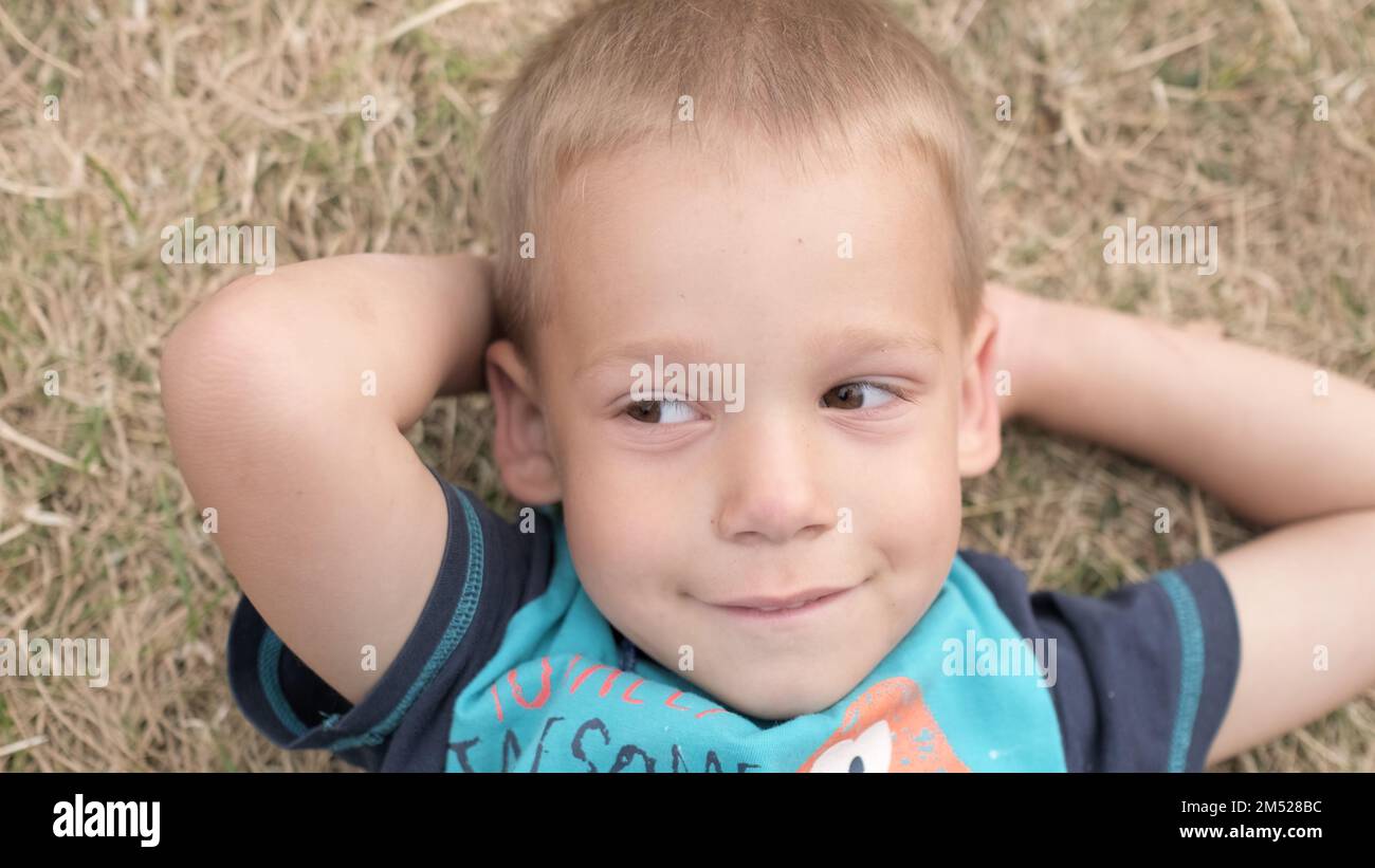 Little Happy Serious and Thoughtful Child Boy Laying on Yellow Lawn Dry