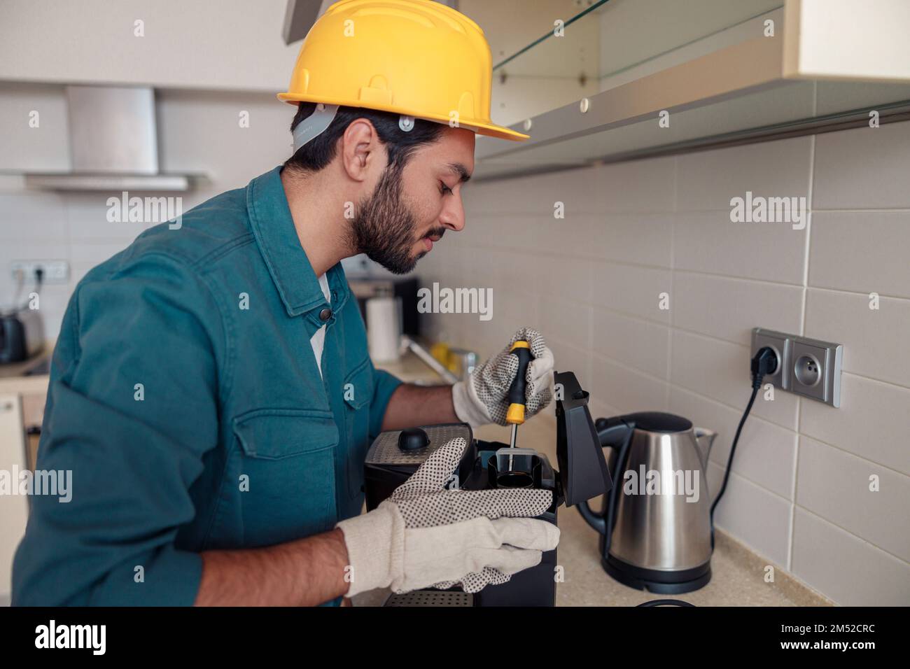 Man with screwdriver fixing coffee machine at table in kitchen