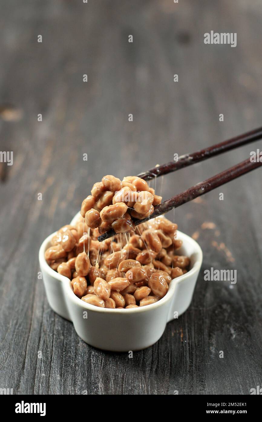 Natto Lifted with Chopstick. Natto is Japanese Fermented Sticky Soy Beans with Stinky Smell. On Wooden Table Stock Photo