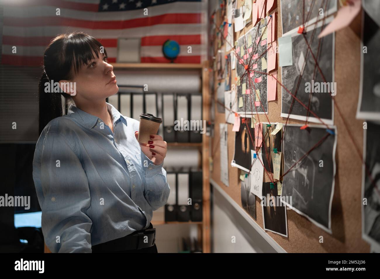 Detective looking at evidence board in her office and drinking coffee. Copy space Stock Photo