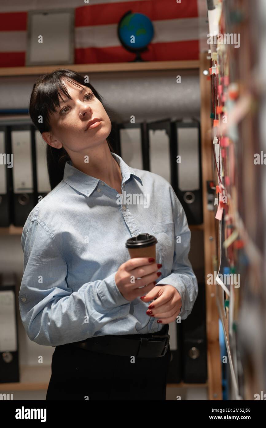 Portrait of female detective looking at evidence board in her office, copy space Stock Photo