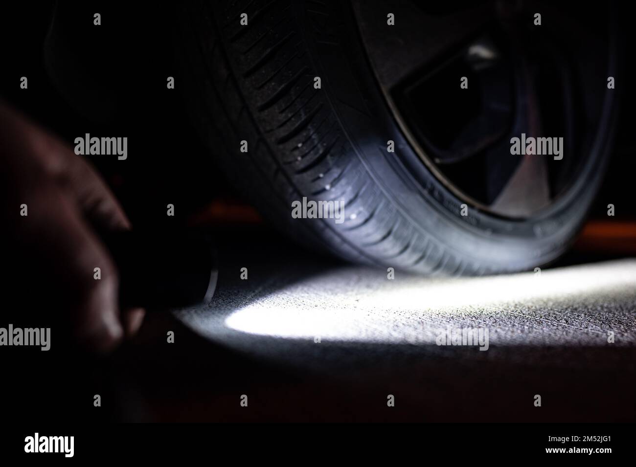 Flashlight pointing towards a vehicle flat tire at night Stock Photo