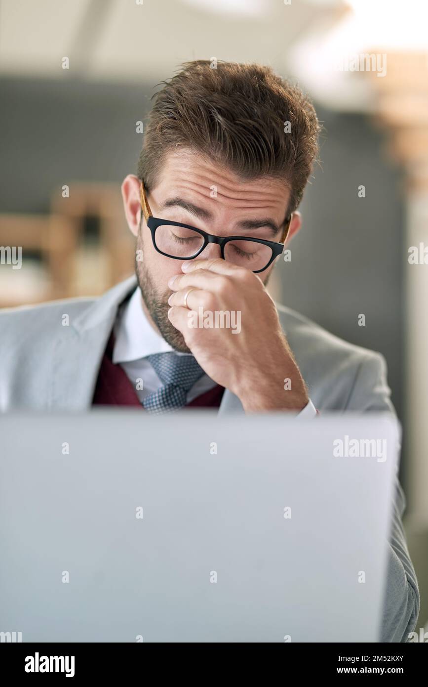 This day isnt doing it for me. a businessman feeling exhausted while using a laptop at his office desk. Stock Photo