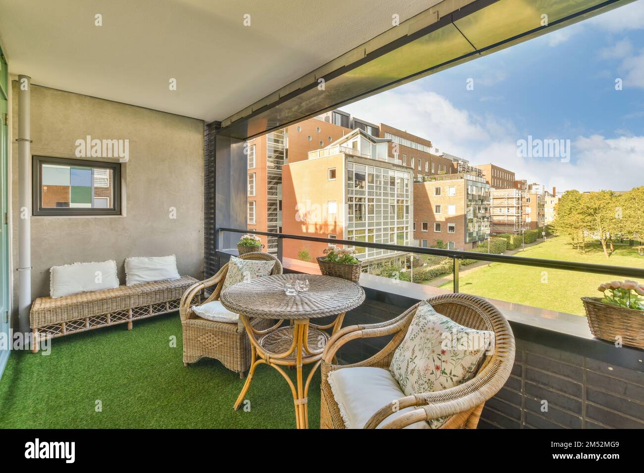 a balcony with two wickers and a table on the left side, looking out onto some buildings in the distance Stock Photo