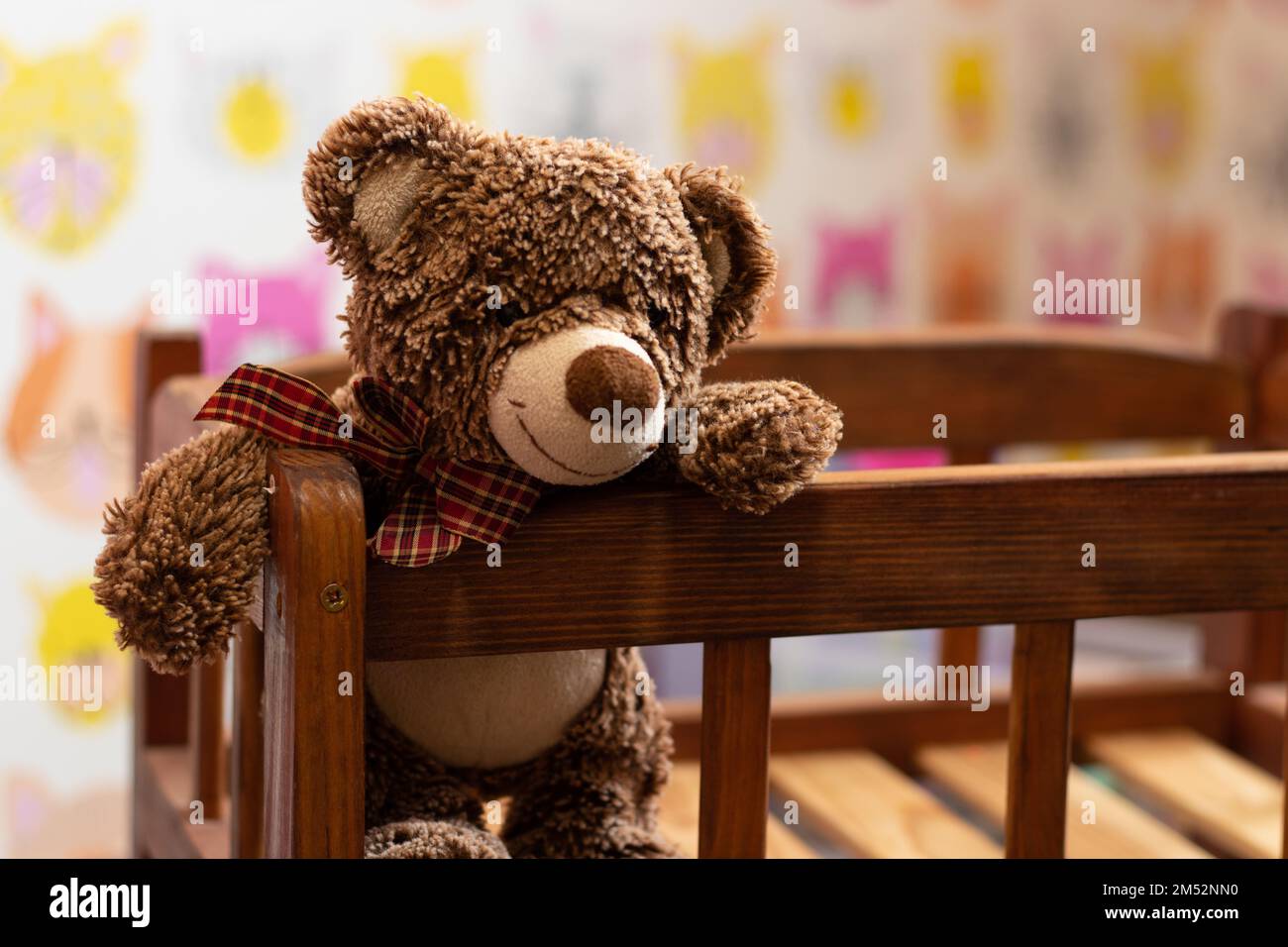 soft brown teddy bear sits in a children's wooden bed in a children's room on a blurred background Stock Photo